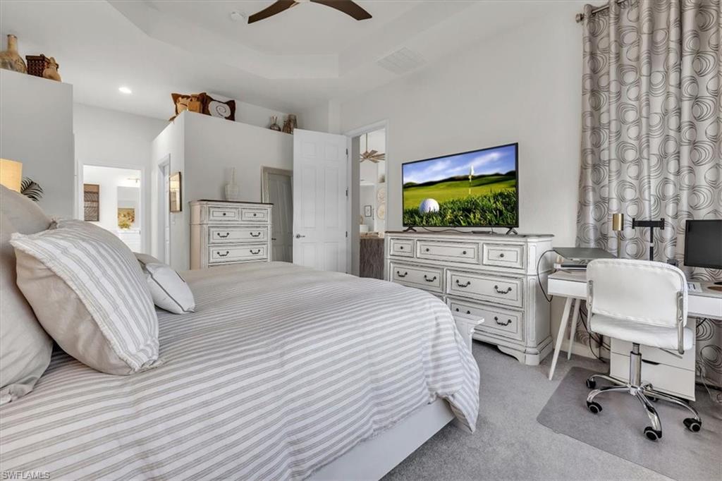 Bedroom featuring a desk, light colored carpet, connected bathroom, a ceiling fan, and a tray ceiling