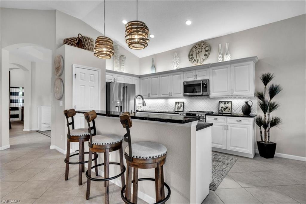 Kitchen with arched walkways, a breakfast bar, high end appliances, a center island with sink, and vaulted ceiling