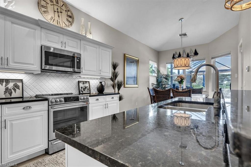 Kitchen featuring stainless steel appliances, dark stone counters, white cabinets, tasteful backsplash, and a chandelier