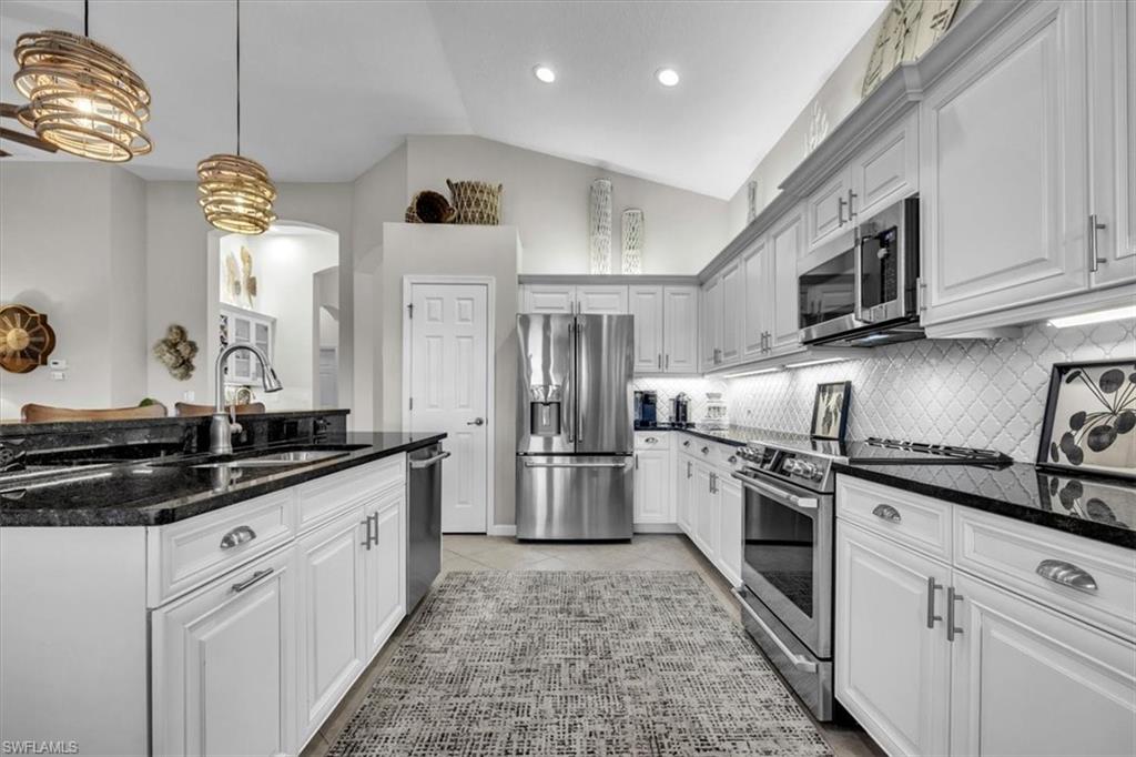 Kitchen with dark stone countertops, lofted ceiling, stainless steel appliances, pendant lighting, and white cabinets