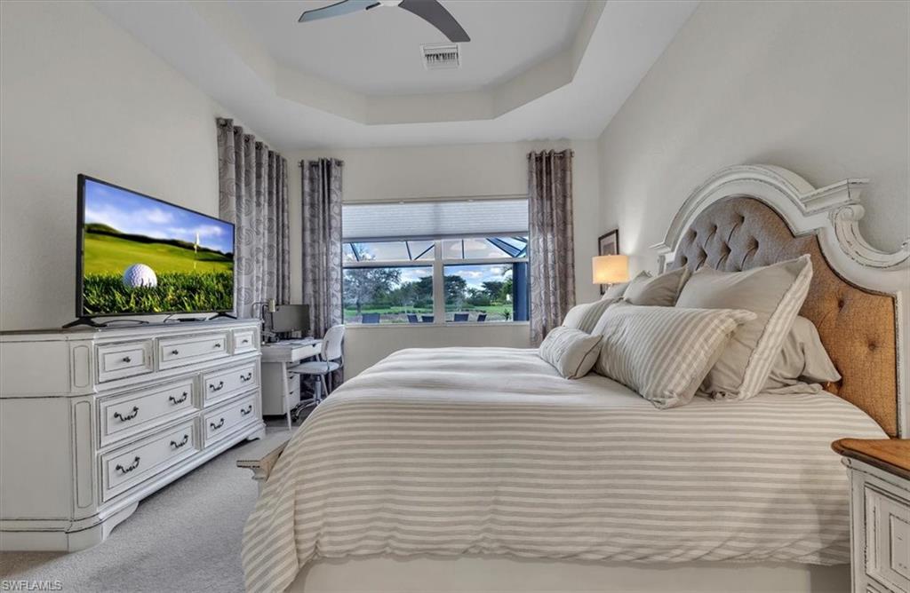 Carpeted bedroom featuring a raised ceiling and ceiling fan