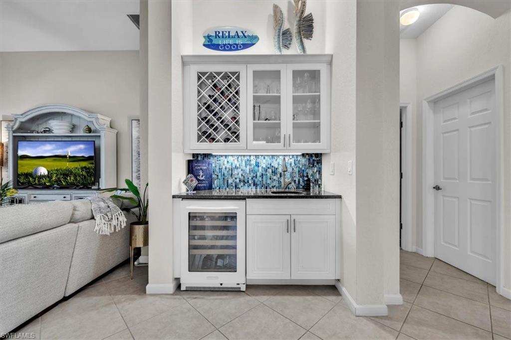 Indoor bar featuring dark stone countertops, white cabinetry, wine cooler, glass fronted cabinets, and tasteful backsplash