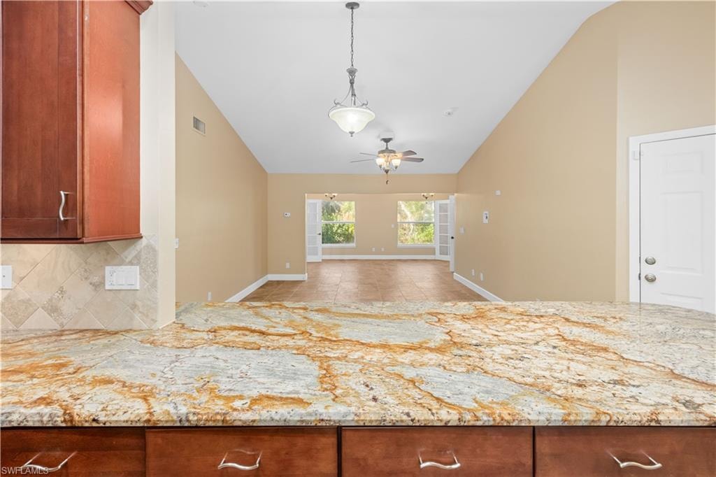 Kitchen with open floor plan, light stone counters, vaulted ceiling, backsplash, and hanging light fixtures
