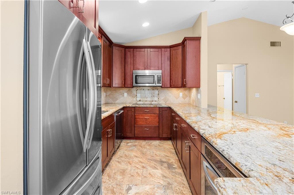 Kitchen with stainless steel appliances, light stone countertops, lofted ceiling, decorative backsplash, and pendant lighting
