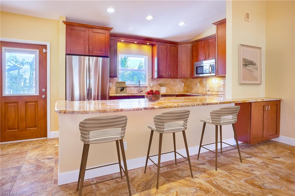 Kitchen with stainless steel appliances, light stone countertops, a breakfast bar area, a peninsula, and backsplash