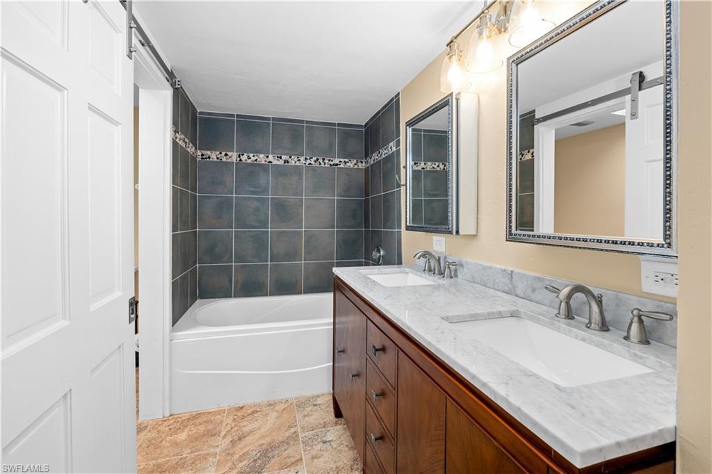 Full bathroom featuring double vanity, light stone finish flooring, and shower / tub combination