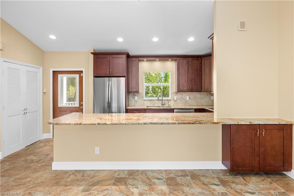 Kitchen featuring a peninsula, freestanding refrigerator, light stone counters, backsplash, and recessed lighting