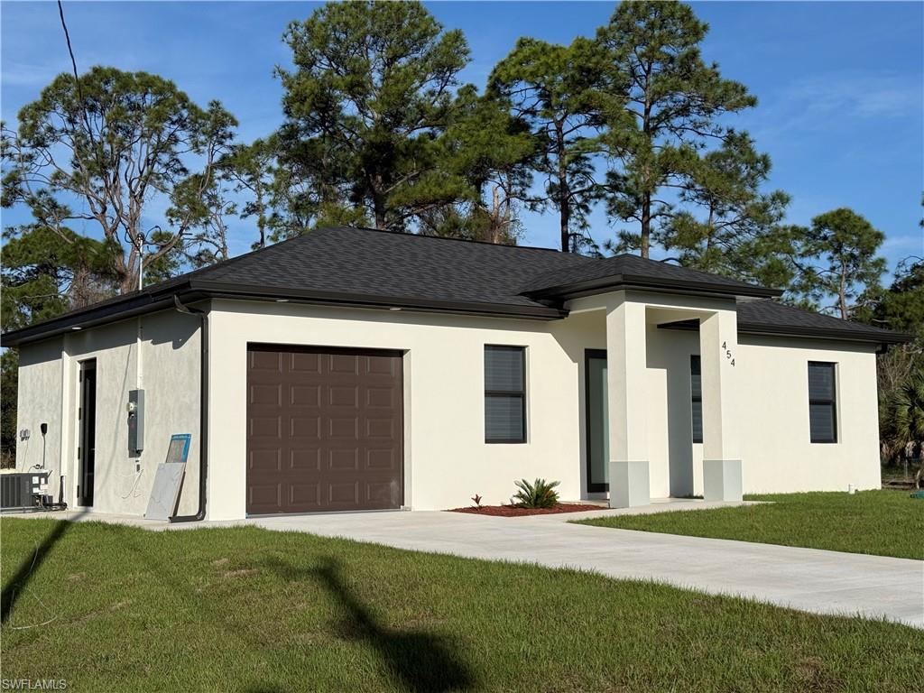 View of front facade with a front lawn, stucco siding, an attached garage, driveway, and roof with shingles