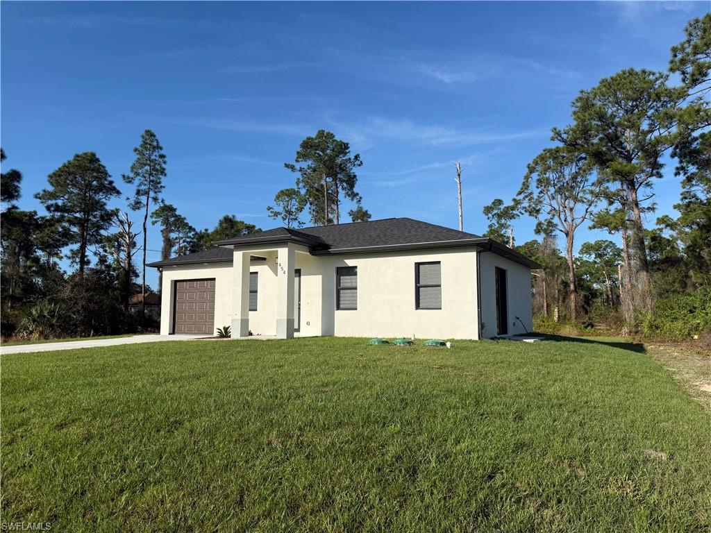 View of front facade with stucco siding, a front yard, a garage, and driveway