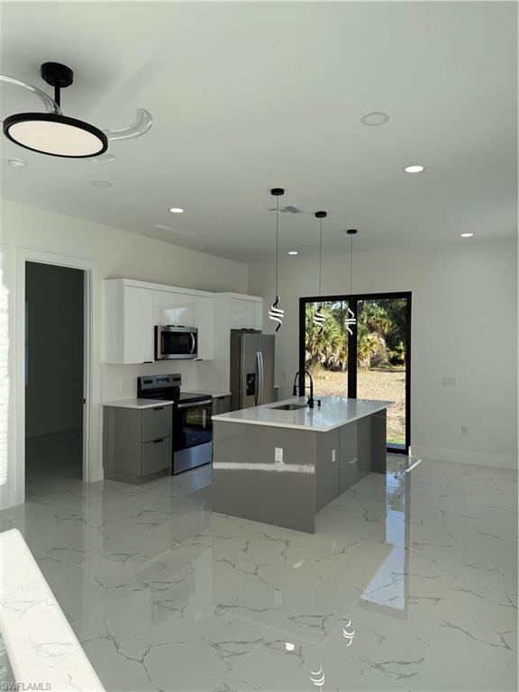 Kitchen featuring dual tone cabinets, range, a center island with sink, stainless steel refrigerator, and hanging light fixtures
