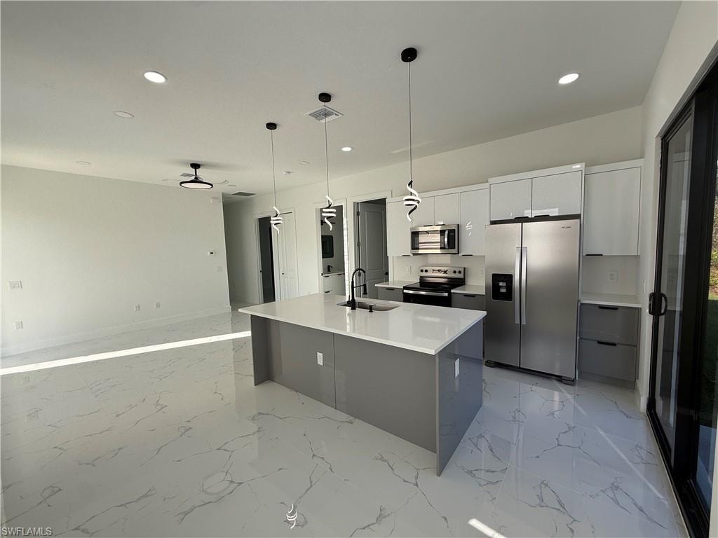 Kitchen with two tone color scheme, stainless steel appliances, hanging light fixtures, an island with sink, and modern cabinets