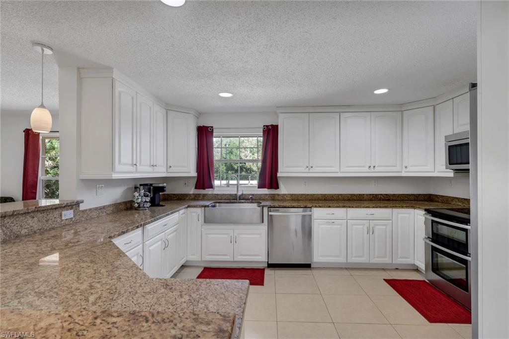 Kitchen featuring white cabinets, stainless steel appliances, dark stone countertops, light tile patterned floors, and a textured ceiling