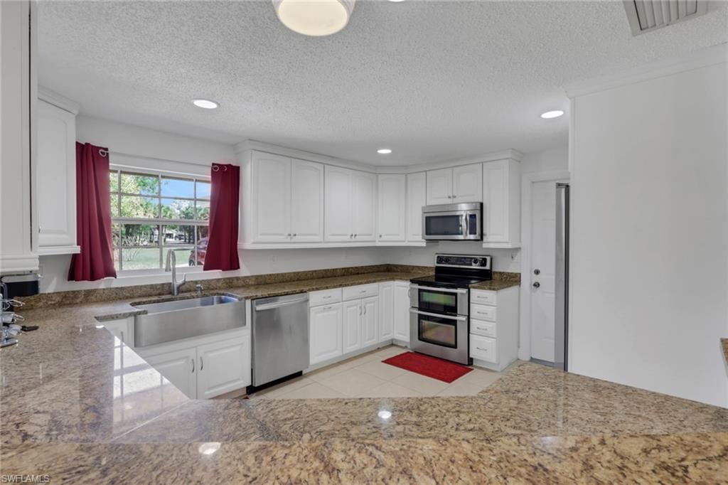 Kitchen with stainless steel appliances, recessed lighting, white cabinets, a textured ceiling, and dark stone countertops