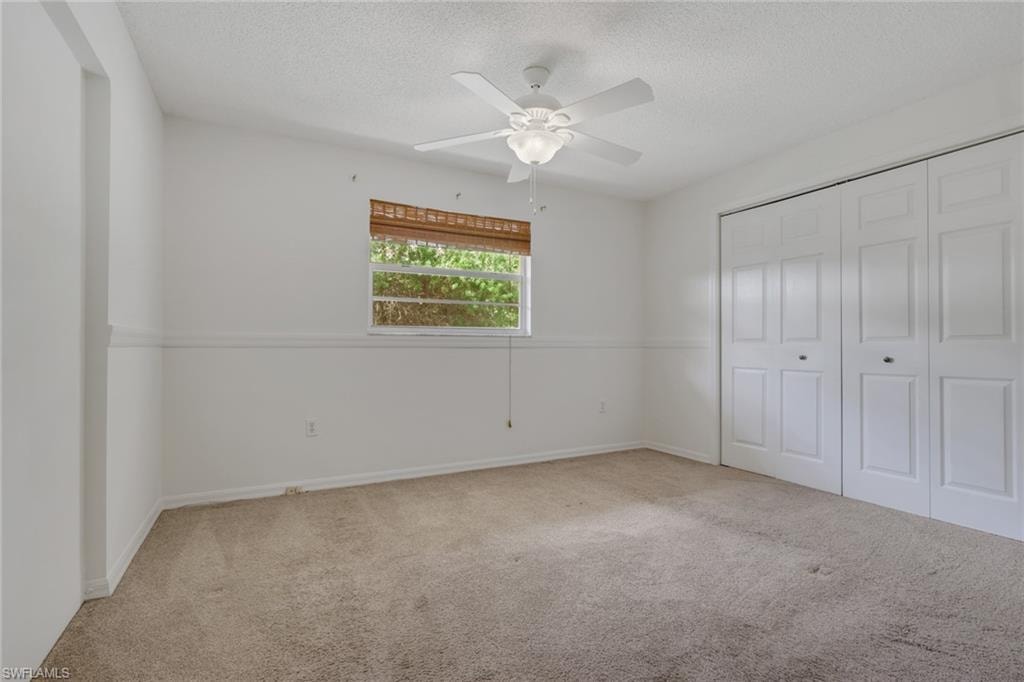 Unfurnished bedroom with carpet, a closet, ceiling fan, and a textured ceiling