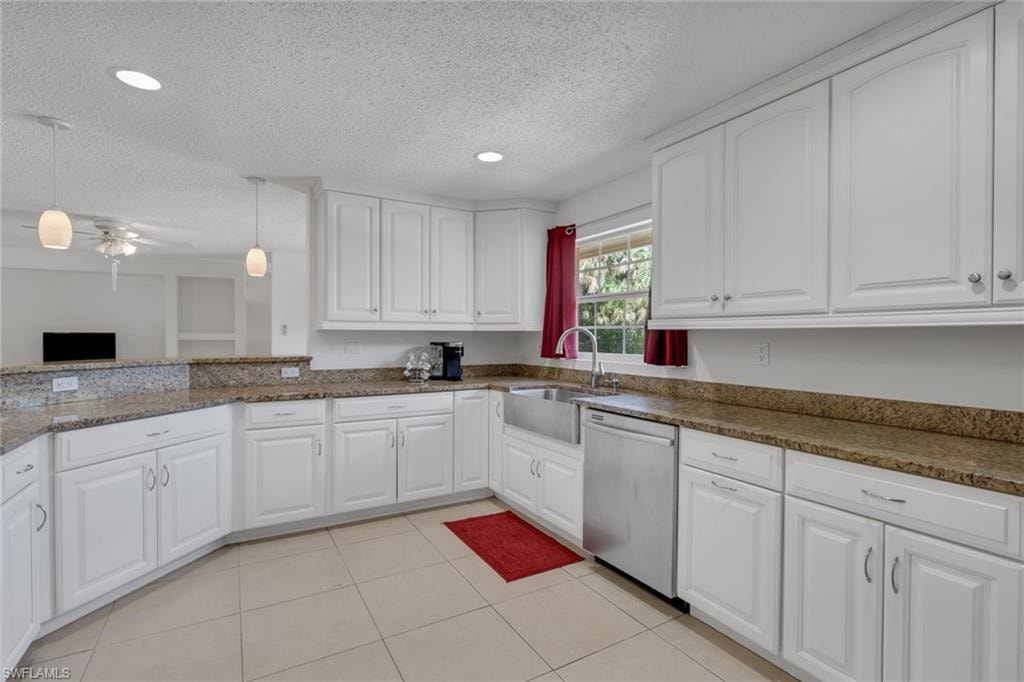 Kitchen with white cabinets, dishwasher, hanging light fixtures, light tile patterned floors, and a textured ceiling