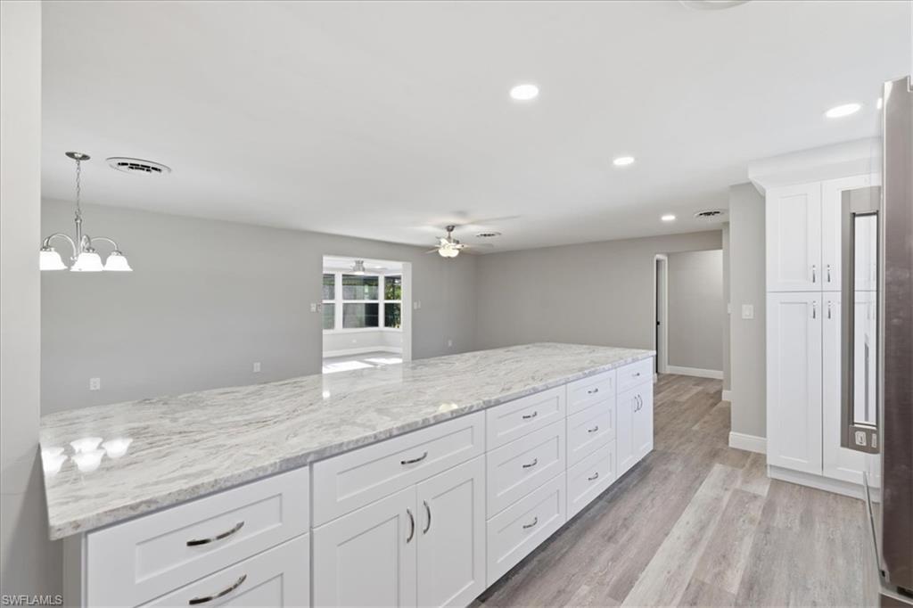Kitchen featuring white cabinetry, light wood-style flooring, light stone counters, a ceiling fan, and hanging lights