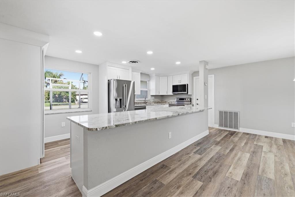 Kitchen featuring white cabinets, light stone countertops, stainless steel appliances, recessed lighting, and light wood-type flooring