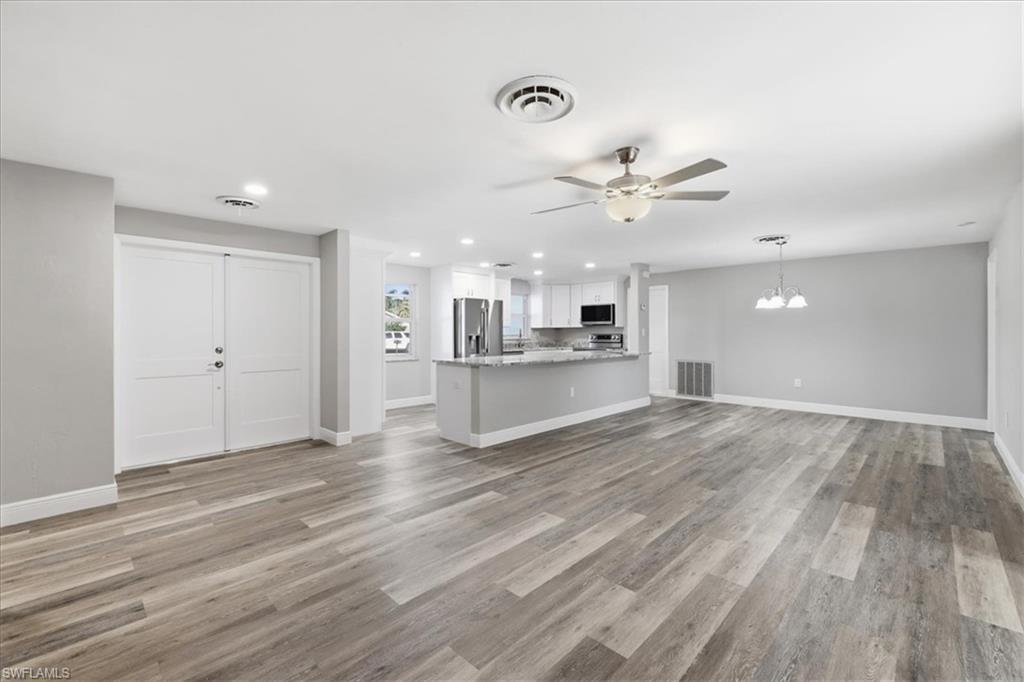 Unfurnished living room with ceiling fan, light wood-type flooring, and a chandelier