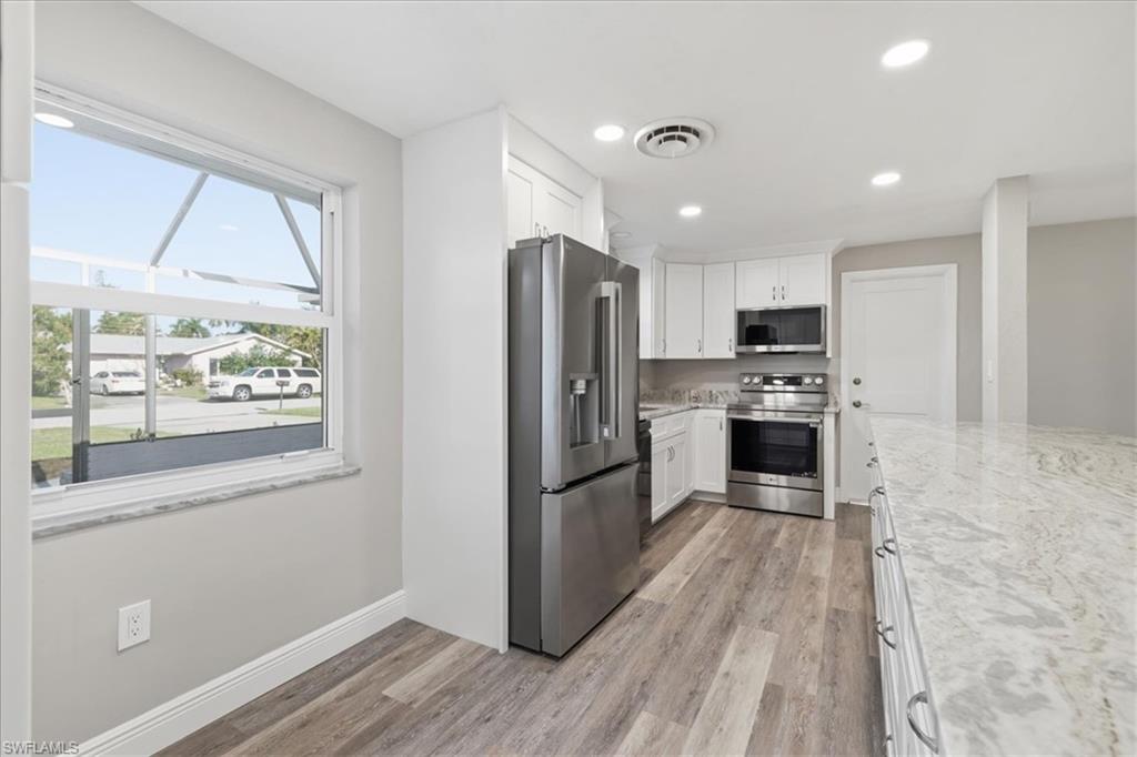 Kitchen with stainless steel appliances, white cabinets, light wood-type flooring, light stone counters, and recessed lighting