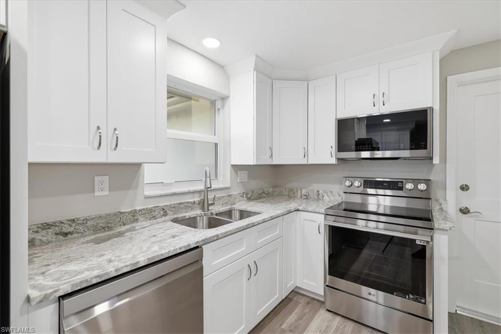 Kitchen featuring stainless steel appliances, white cabinetry, light stone counters, light wood finished floors, and recessed lighting