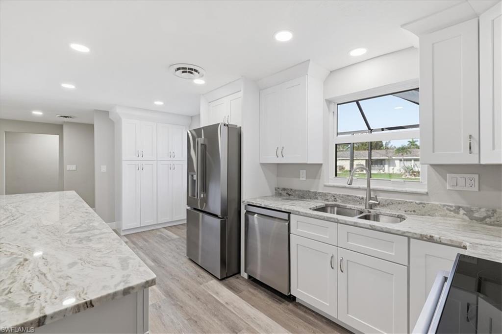Kitchen featuring stainless steel appliances, light stone countertops, white cabinetry, light wood finished floors, and recessed lighting