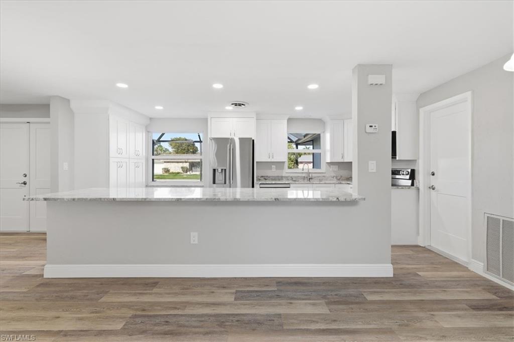 Kitchen island featuring light stone counters, stainless steel appliances, white cabinets, a peninsula, and light wood finished floors
