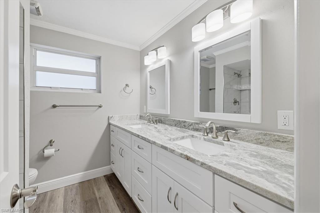 Full Guest bath with crown molding, double vanity, a shower, and dark wood-style flooring