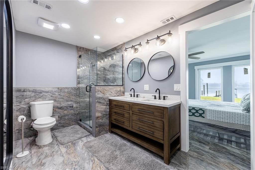 Ensuite bathroom featuring double vanity, a marble finish shower, tile walls, recessed lighting, and wainscoting