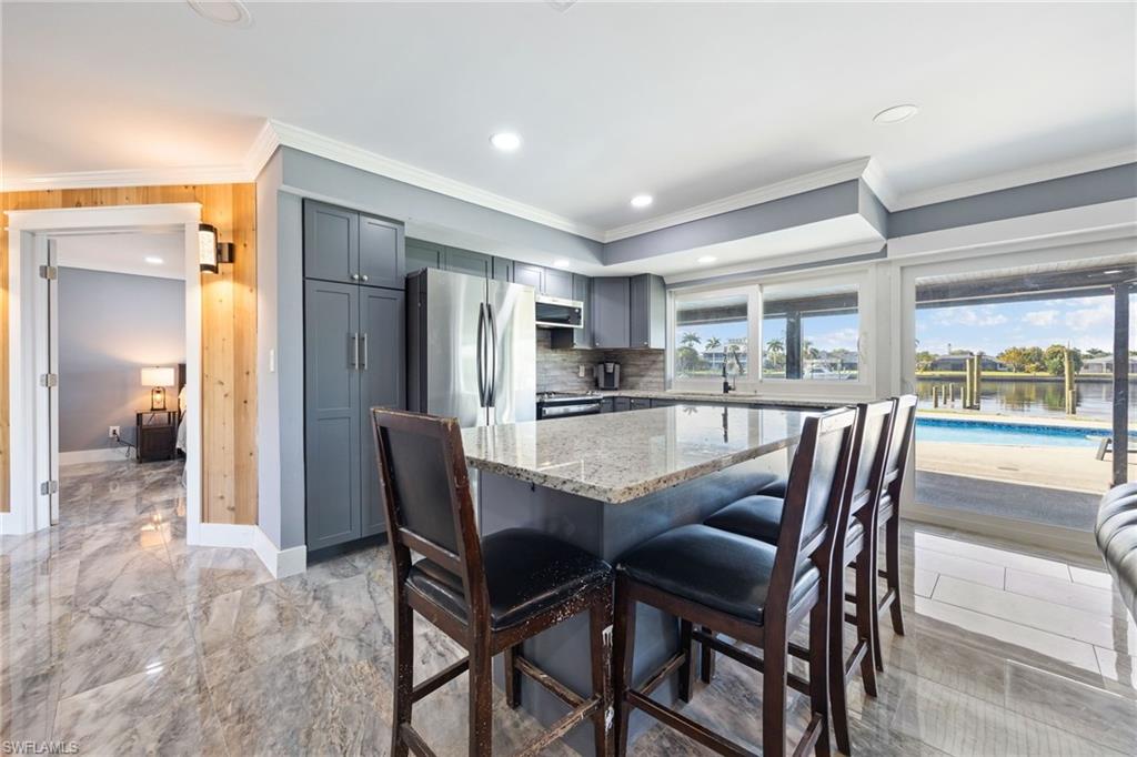 Kitchen with gray cabinetry, stainless steel appliances, light stone counters, a center island, and a breakfast bar