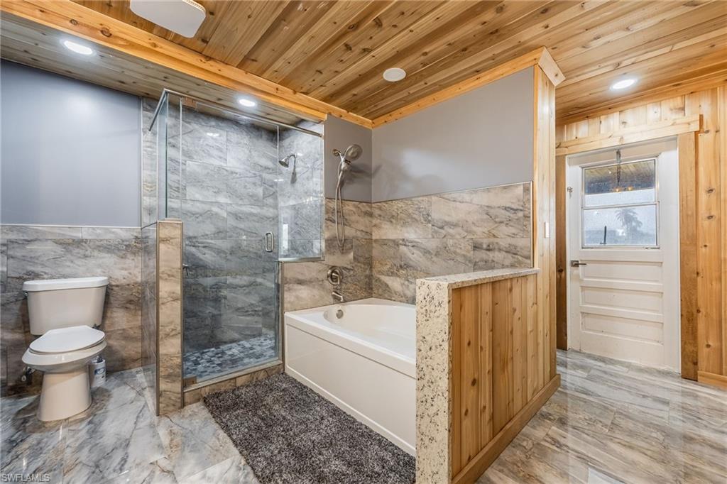 Full bath with light marble finish floors, a garden tub, a marble finish shower, tile walls, and a wainscoted wall
