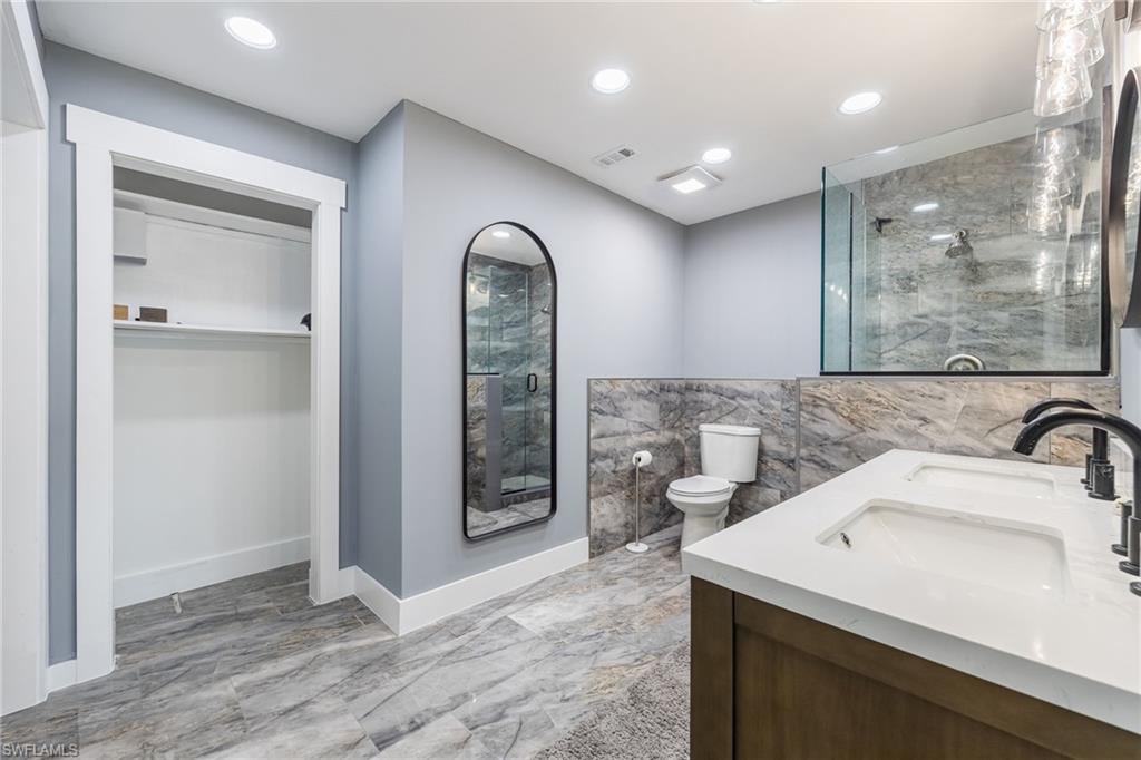 Bathroom with double vanity, a marble finish shower, a walk in closet, recessed lighting, and light marble finish floors