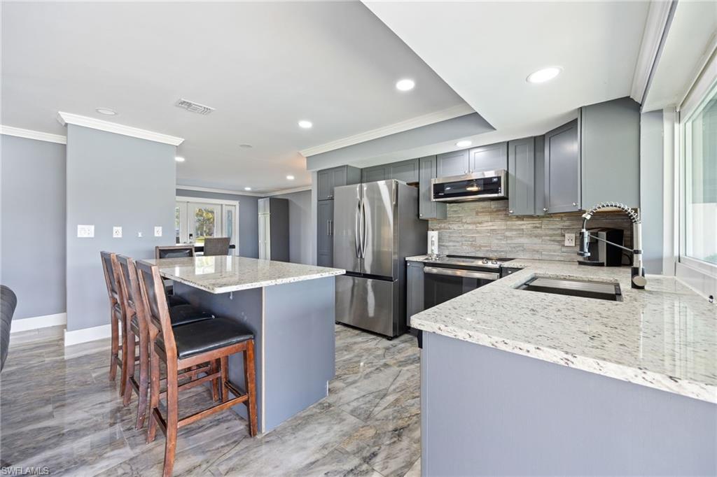 Kitchen with light stone counters, gray cabinets, a kitchen bar, stainless steel appliances, and crown molding