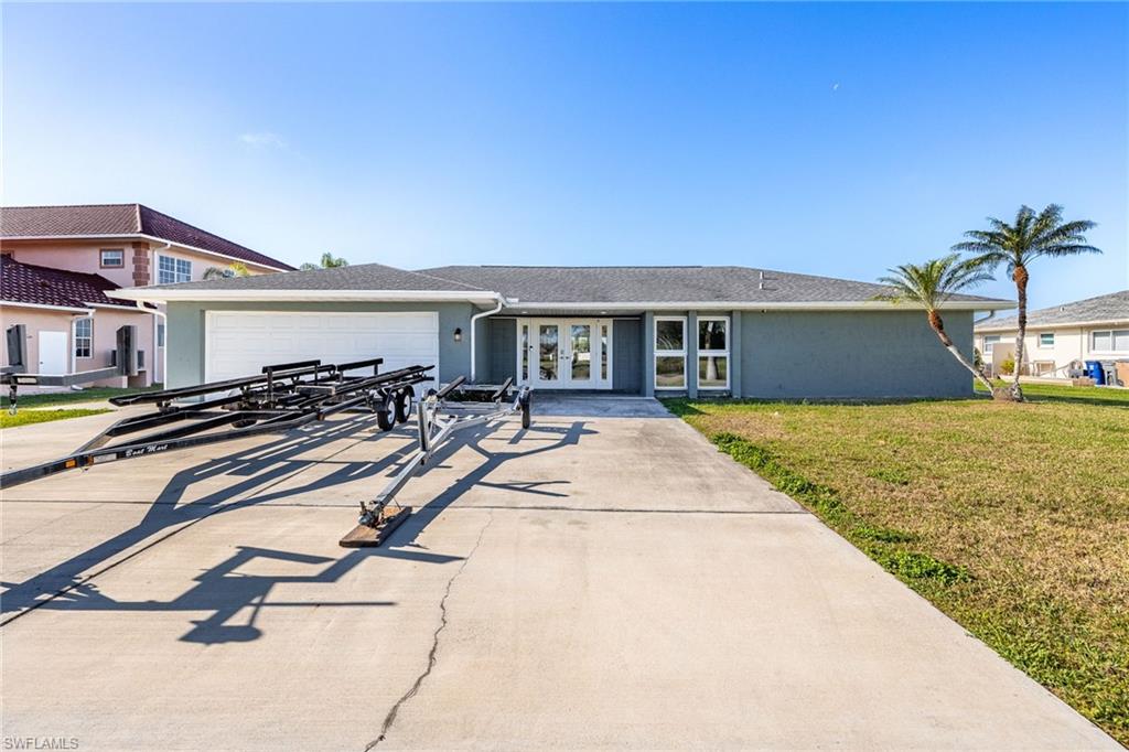 View of front of house featuring french doors, an attached garage, driveway, and a front lawn