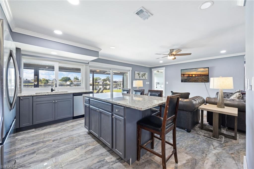 Kitchen with a breakfast bar area, light stone countertops, ornamental molding, stainless steel appliances, and a kitchen island