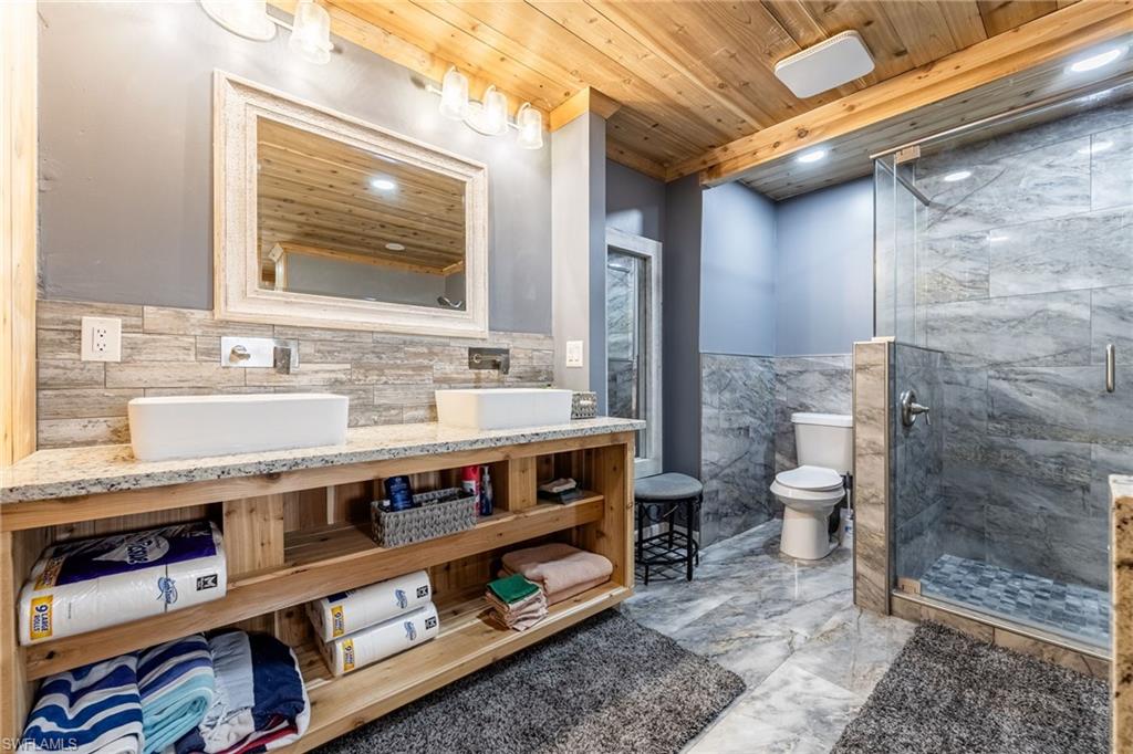 Full bathroom with wainscoting, tile walls, vanity, wooden ceiling, and a shower stall