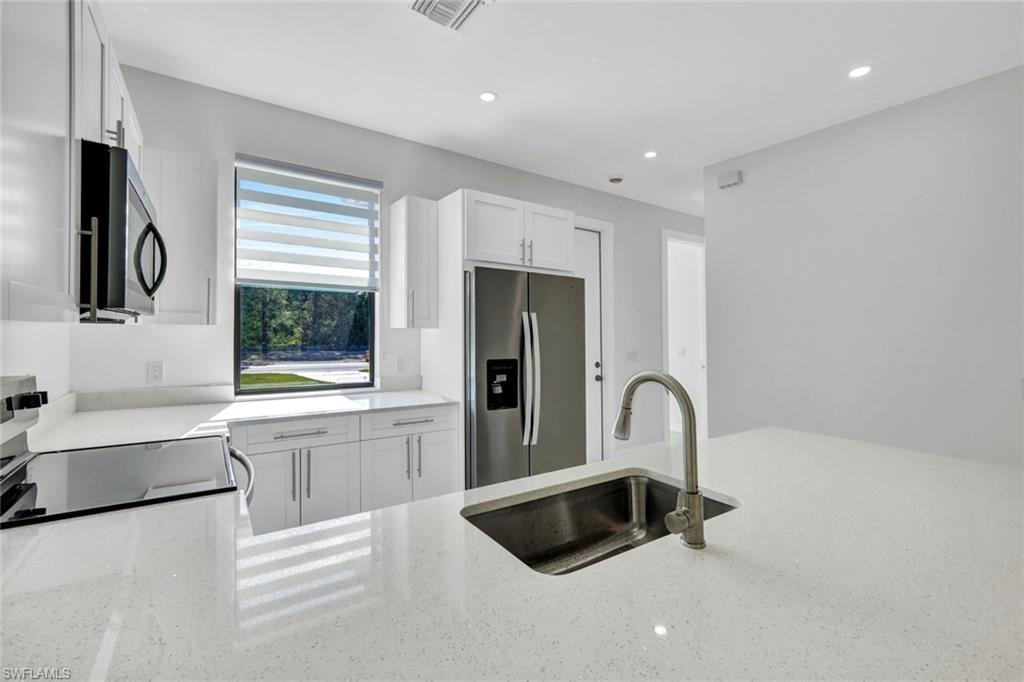 Kitchen with stainless steel refrigerator with ice dispenser, white cabinets, light stone countertops, recessed lighting, and range with electric stovetop