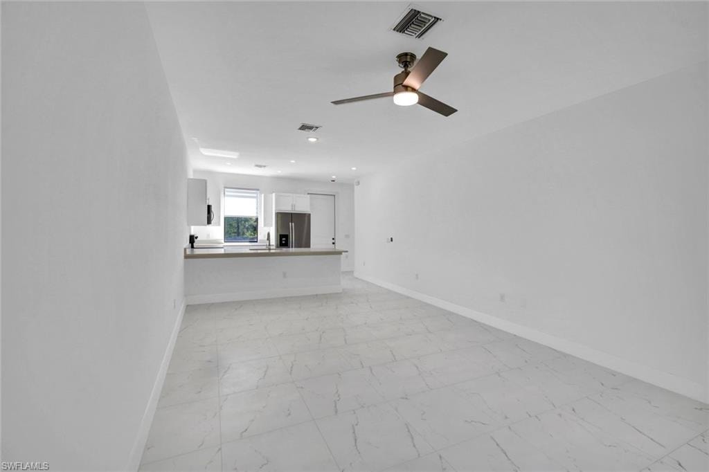 Unfurnished living room featuring light marble finish floors and ceiling fan
