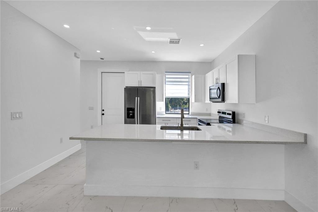 Kitchen featuring a peninsula, light stone counters, stainless steel appliances, white cabinetry, and light marble finish floors
