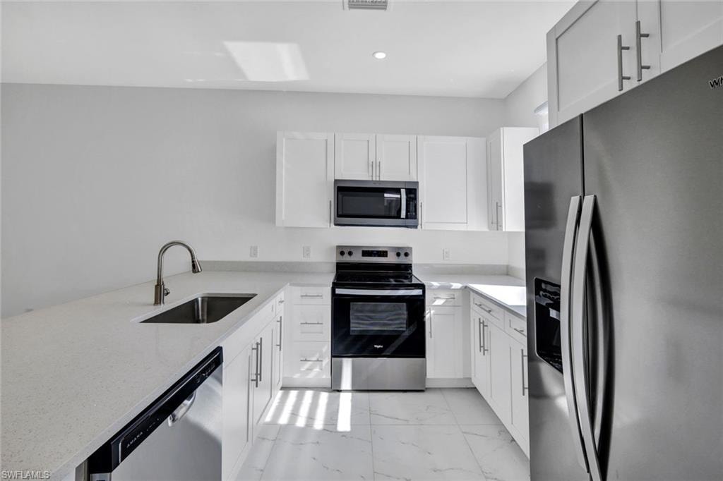 Kitchen featuring stainless steel appliances, light marble finish flooring, light stone counters, and white cabinetry