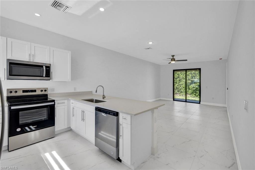 Kitchen with stainless steel appliances, light marble finish flooring, white cabinets, a peninsula, and recessed lighting