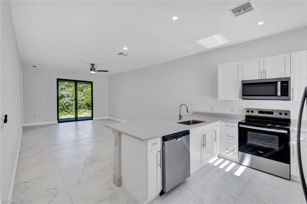 Kitchen featuring stainless steel appliances, light marble finish flooring, a peninsula, white cabinetry, and light stone countertops