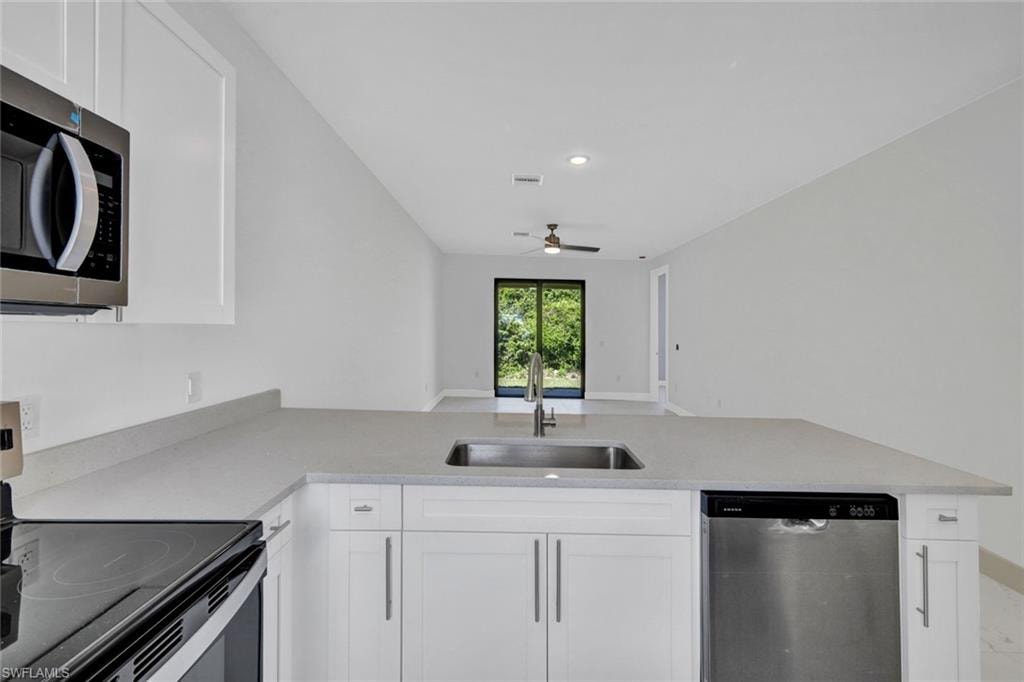 Kitchen featuring stainless steel appliances, white cabinetry, a peninsula, light stone counters, and open floor plan