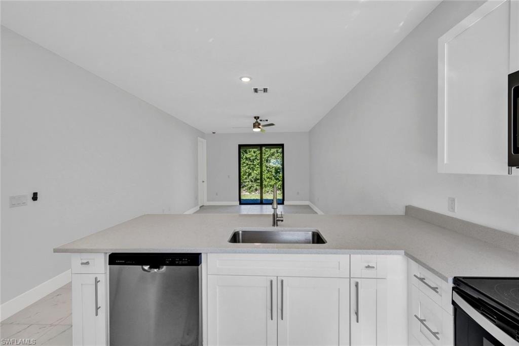 Kitchen featuring dishwasher, a peninsula, white cabinetry, light stone counters, and a ceiling fan