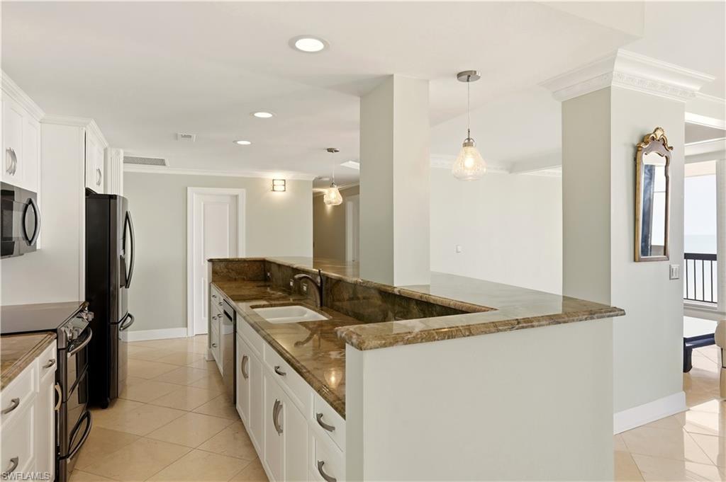 Kitchen with white cabinetry, black appliances, ornamental molding, light tile patterned flooring, and dark stone counters