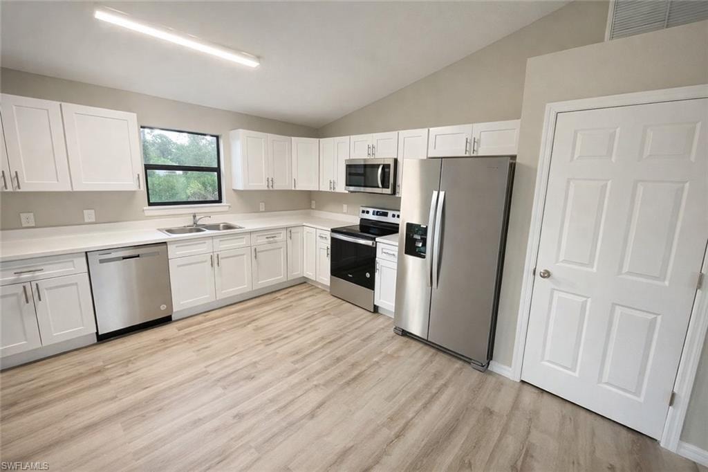 Kitchen featuring stainless steel appliances, vaulted ceiling, white cabinetry, light countertops, and light wood-style flooring