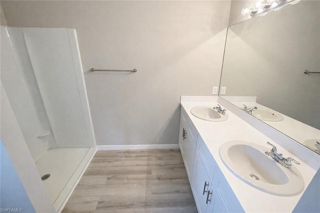 Bathroom with double vanity, light wood-style flooring, and a shower stall