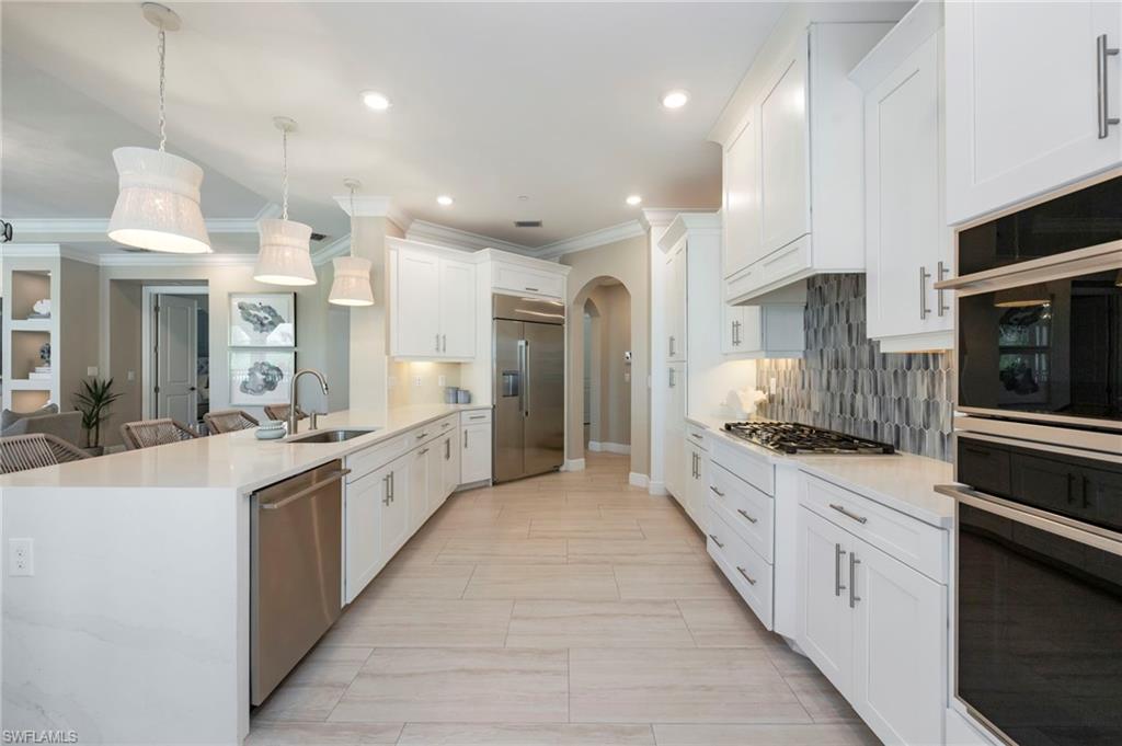 Kitchen featuring arched walkways, light stone counters, stainless steel appliances, a peninsula, and ornamental molding