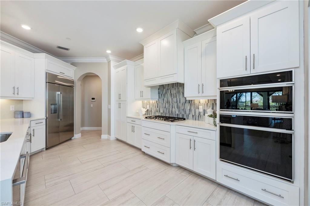 Kitchen featuring stainless steel appliances, arched walkways, white cabinets, light stone countertops, and ornamental molding