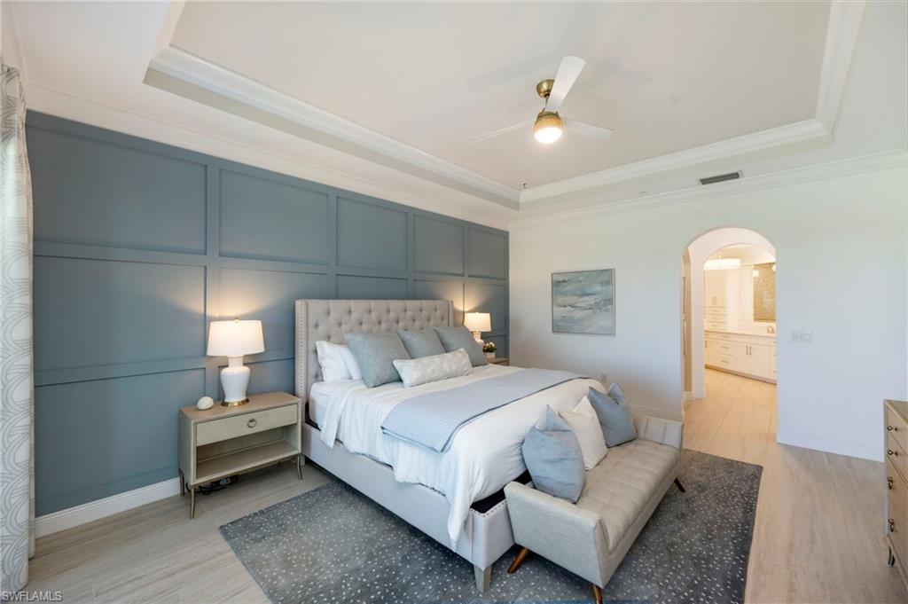 Bedroom with a decorative wall, a raised ceiling, light wood-style floors, arched walkways, and ceiling fan