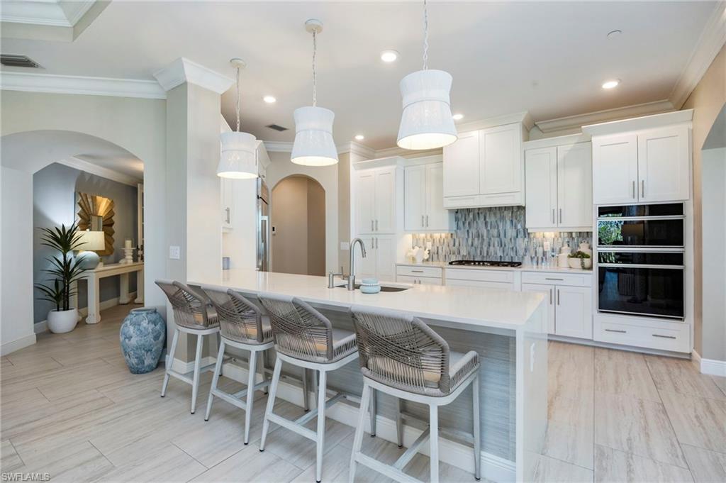 Kitchen with a breakfast bar, arched walkways, white cabinets, tasteful backsplash, and a peninsula
